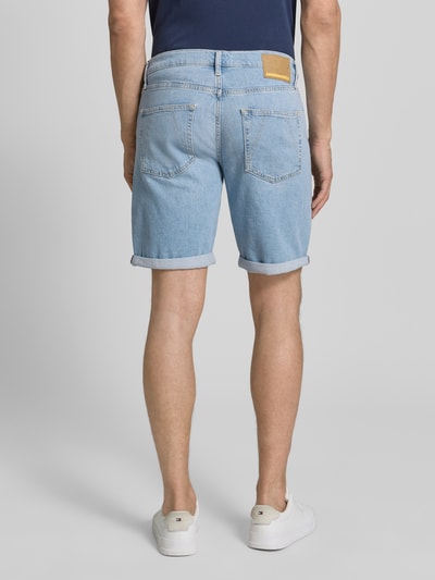 Männermodel trägt Slim Fit Jeansshorts aus Baumwoll-Mix Modell 'NAAILO' von Armedangels in Denim-Optik mit Label-Patch, 5-Pocket-Design, hellblaue Farbe, Beinabschluss mit Umschlag, Ganzkörperansicht Rückansicht.