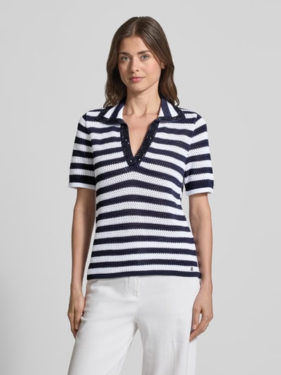 Frauenmodel trägt Regular Fit Poloshirt in Strick-Optik von monari, navy-weiß gestreift, Halbarm, Ziersteinbesatz, Ganzkörperansicht von vorne.