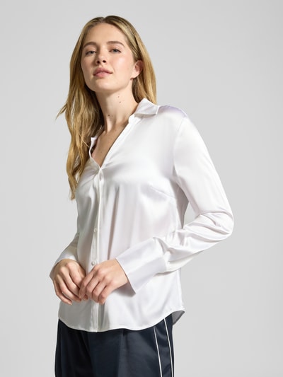Modelka kobieca ma na sobie Bluse aus Satin mit V-Ausschnitt von HERZENS, kolor biały, krój regular fit, z kołnierzem koszulowym, satynowa tekstura, długość tyłu 64 cm, długość rękawa 60 cm, ujęcie całej sylwetki z przodu.