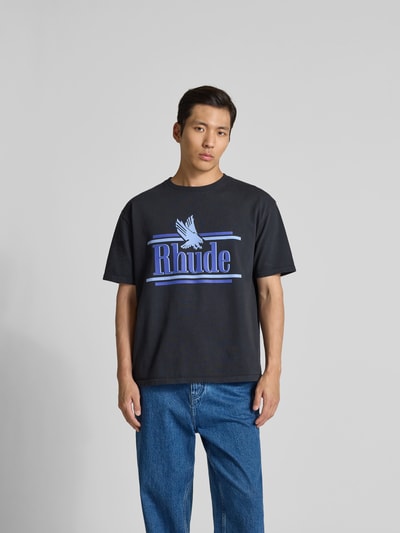 Männermodel trägt Regular Fit T-Shirt aus reiner Baumwolle von RHUDE, schwarzer Stoff, blauer Label-Print, Rundhalsausschnitt, Ganzkörperansicht von vorne. Herren T-Shirt, Rückenlänge bei Größe M: 70 cm, kurzärmeliges Design.