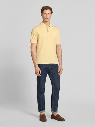 Männermodel trägt Regular Fit Poloshirt mit Brusttasche und Label-Stitching von bugatti in Gelb, kombiniert mit Jeans; Ganzkörperansicht von vorne. Rückenlänge bei Größe M: 70 cm, Knopfleiste, Polokragen.