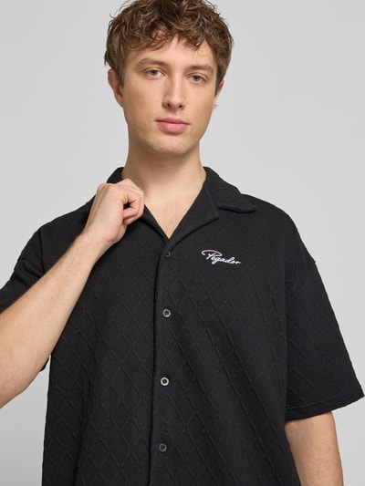 Männermodel trägt Regular Fit vrijetijdsoverhemd met labelstitching model 'Jovren' van Pegador in zwart, elastische materiaalmix met katoen, reverskraag, halflange mouwen, knoopsluiting, textuur met ruitpatroon, Nahaufnahme Oberkörper.