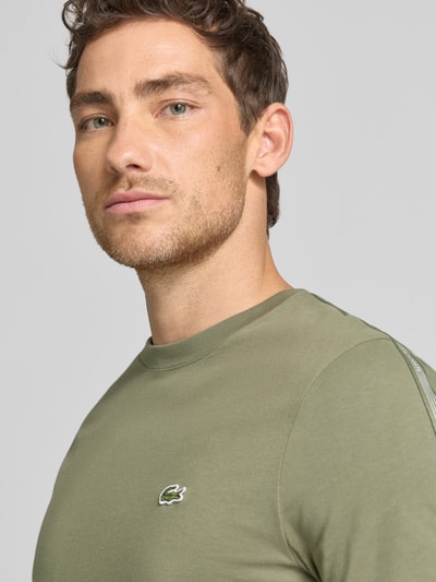 Männermodel trägt Regular Fit T-Shirt aus reiner Baumwolle von Lacoste, unifarben in Olivgrün, Label-Tape, Rundhals, Nahaufnahme Oberkörper.