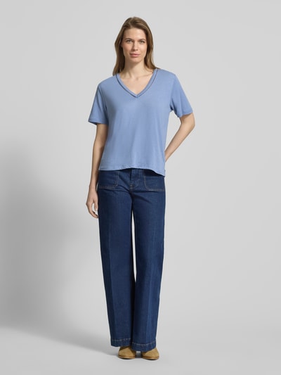 Frauenmodel trägt Relaxed Fit T-Shirt aus Leinen-Mix mit V-Ausschnitt von Scotch & Soda in Hellblau mit Lochmuster, Ganzkörperansicht von vorne.