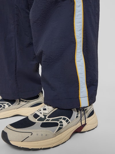 Männermodel trägt Trackpants mit Label-Stitching Modell 'SLIPSTREAM' von PROHIBITED, dunkelblau mit hellem Streifen, Nahaufnahme Bein. Relaxed Fit, elastischer Bund, Innenbeinlänge bei Größe M: 74 cm.