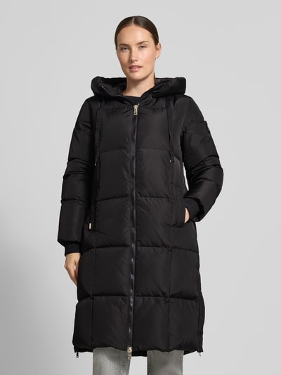 Frauenmodel trägt Regular Fit Mantel in Stepp-Optik Modell 'Nova' von MOS MOSH in Schwarz, Kapuze, Zweiwege-Reißverschluss, Eingrifftaschen, Ganzkörperansicht von vorne.
