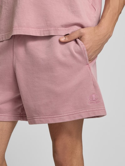 Männermodel trägt Sweatshorts mit Eingrifftaschen von CHAMPION in Rosa, Baumwoll-Mix, Regular Fit, Label-Stitching, Nahaufnahme Oberschenkel.