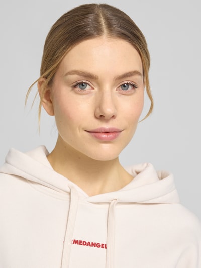 Vrouwenmodel draagt Oversized Hoodie uit puur katoen model 'FRANCISARAA DIFFERENCE' van Armedangels, effen sweatstof met capuchon, label-opdruk, kangoeroezak, geribde boorden, detailopname bovenlichaam.
