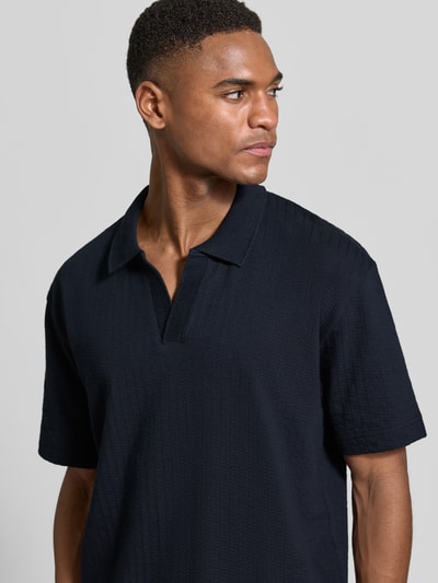 Männermodel trägt Relaxed Fit Poloshirt aus reiner Baumwolle von Marc O'Polo in Dunkelblau, strukturierte Weboptik, Nahaufnahme Oberkörper.