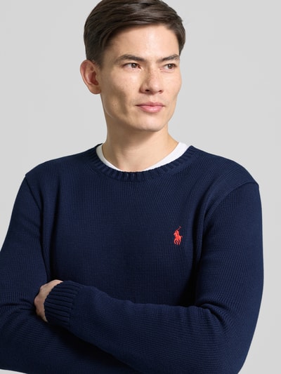 Męski model nosi Sweter z dzianiny z prążkowanymi wykończeniami od Polo Ralph Lauren, bawełna, krój regular fit, okrągły dekolt, wyhaftowane logo, długość tyłu 67 cm, długość rękawów 66 cm, kolor ciemnogranatowy, faktura gładka i miękka, nahaufnahme górnej części ciała.
