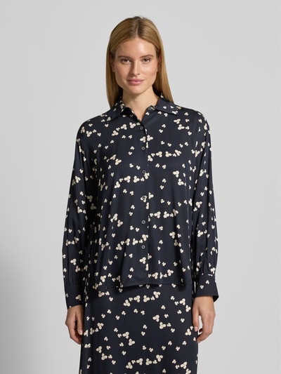 Vrouwenmodel draagt Oversized Langarmbluse aus reiner Viskose van Marc O'Polo met florale print, donkerblau met lichte details, rechte twill stof, knoopsluiting, borstzak, lange mouwen met manchetten, asymmetrische zoom, zijsplitten, uni-optiek, label stitching. Vooraanzicht bovenlichaam.