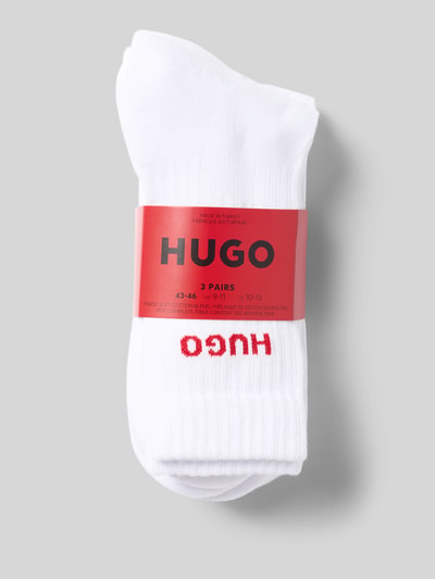 Produktfoto, witte sokken van HUGO, effen design, zacht katoen, rode HUGO-logo, verpakking met label, drie paar, geribde textuur