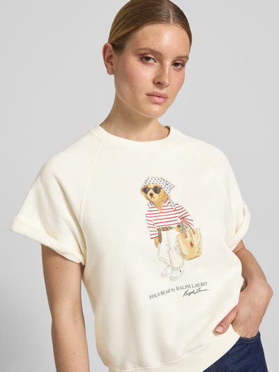 Kobiece model prezentuje Regular Fit Sweatshirt mit Polo Bear Print von Polo Ralph Lauren w efekcie: jednolity kolor, aplikacja: nadruk polo bear, krój: krój regular fit, kształt kołnierza: okrągły dekolt, rękaw: raglanowe rękawy, zakończenie rękawów: prążkowane, wykończenie materiału: dzianina dresowa, materiał: mieszanka bawełny, jasny kolor, gładka tekstura. Nahaufnahme górnej części ciała z przodu.