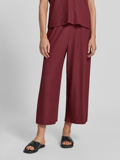 Frauenmodel trägt Loose Fit Hose in Crinkle-Optik von s.Oliver RED LABEL in Dunkelrot, strukturierte Oberfläche, Nahaufnahme Unterkörper.