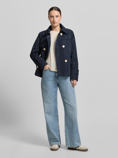 Frauenmodel trägt Jacke mit Ärmelriegeln von Amber & June in Dunkelblau, cremefarbenes Shirt, Jeans, Zweireiher, Eingrifftaschen, Ganzkörperansicht von vorne.