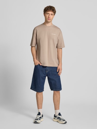 Männermodel trägt Oversized T-Shirt mit Label-Stitching von Pegador, Baumwoll-Mix, Rundhalsausschnitt, beige Farbe, Ganzkörperansicht von vorne.