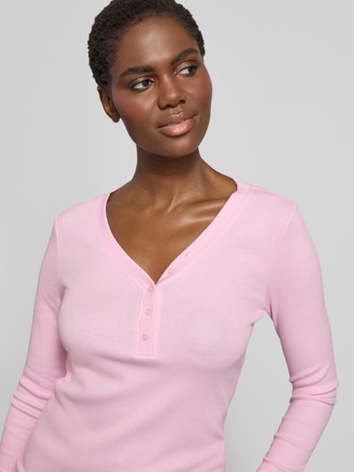 Modelka kobieca ma na sobie Slim Fit Bluzkę z długim rękawem z ozdobną listwą guzikową od s.Oliver RED LABEL, melanż, dekolt w serek, prążkowana faktura, wykończenie materiału: ripp, aplikacja: ozdobna listwa guzikowa, kolor różowy, zbliżenie na górną część ciała.