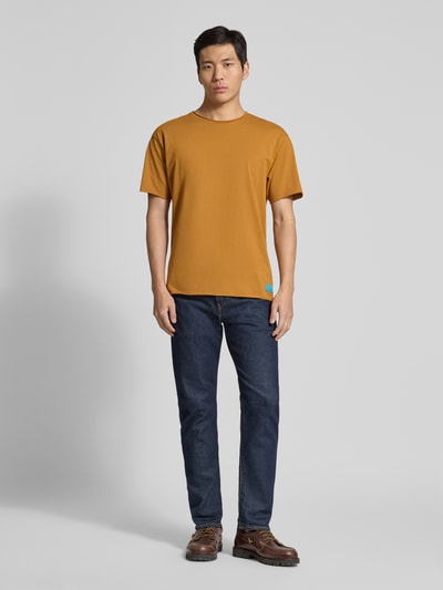 Männermodel trägt T-Shirt mit Rundhalsausschnitt und Label-Detail von Scotch & Soda, reine Baumwolle, Regular Fit, Rollsaum, Ganzkörperansicht von vorne.