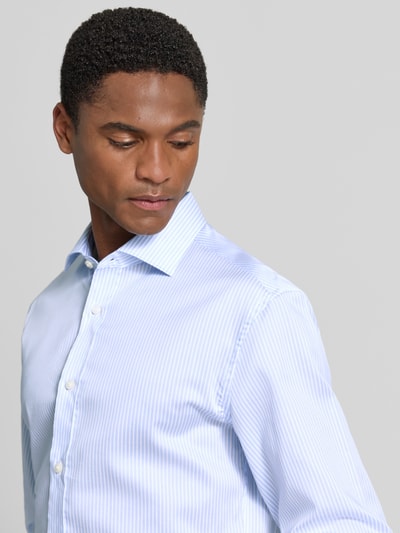 Męskimodel nosi koszulę casualową Slim Fit Freizeithemd mit Kentkragen model 'Adley' od Tiger Of Sweden z bawełny, krój slim fit, kołnierzyk typu kent, długie rękawy, pełna listwa guzikowa, długość tyłu w rozmiarze 40: 79 cm, szerokość w rozmiarze 40: 49 cm, długość rękawów w rozmiarze 40: 68 cm, jasnoniebieskie prążki, zbliżenie na górną część ciała, widok z przodu