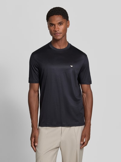 Männermodel trägt T-Shirt aus Lyocell-Mix mit Label-Stitching von Emporio Armani, schwarz, dezenter Glanz, taillierte Passform, Ganzkörperansicht von vorne.