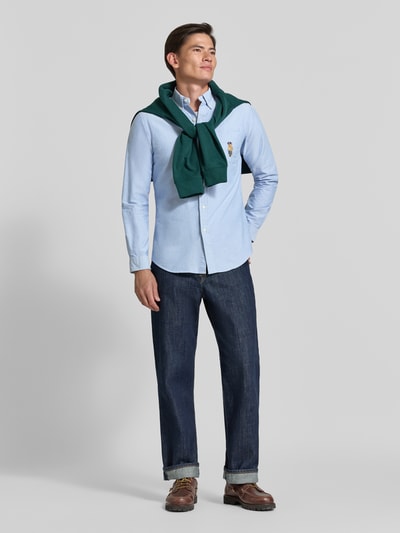 Männermodel trägt Custom Fit Freizeithemd aus reiner Baumwolle von Polo Ralph Lauren in Hellblau, kombiniert mit blauer Jeans, Ganzkörperansicht von vorne.