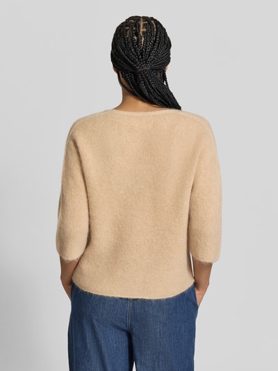 Vrouwenmodel draagt wollen trui uit mix van alpaca en wol van Juvia, beige, losse pasvorm, tricotlook, 3/4-mouw, rolzoom, rugaanzicht.
