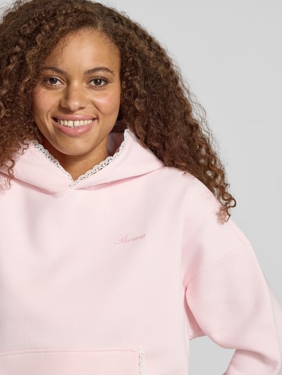 Frauenmodel trägt Hoodie mit Häkelspitzenbesatz von REVIEW in Hellrosa mit Logo-Print, Baumwollmischung, Nahaufnahme Oberkörper.