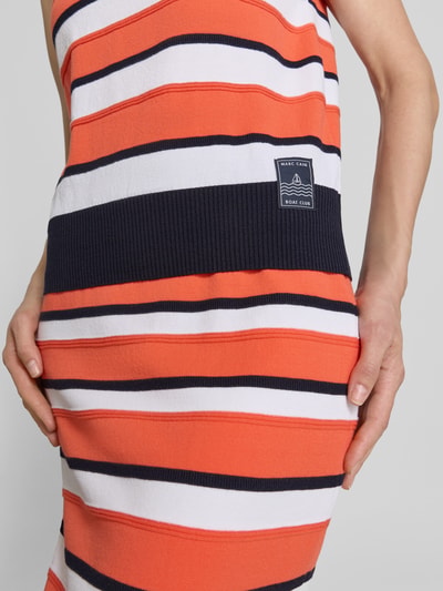 Frauenmodel trägt Pullunder aus Lyocell-Mix im Allover-Look von Marc Cain in Orange, Weiß und Dunkelblau mit Label-Detail, Nahaufnahme Oberkörper.