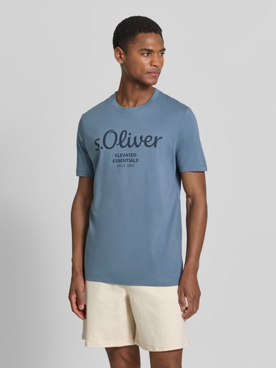 Męski model nosi Regular Fit T-Shirt aus reiner Baumwolle od s.Oliver RED LABEL, kolor jednolity, krój regular fit, nadruk z logo, okrągły dekolt, krótki rękaw, dżersej, czysta bawełna, widok całej sylwetki z przodu.