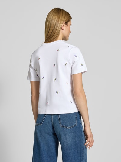 Modelka kobieta ma na sobie T-Shirt mit Blumenstickerei od Christian Berg Woman, biała bawełna z haftem kwiatowym, prosty krój, krótkie rękawy, widok całej sylwetki z tyłu.