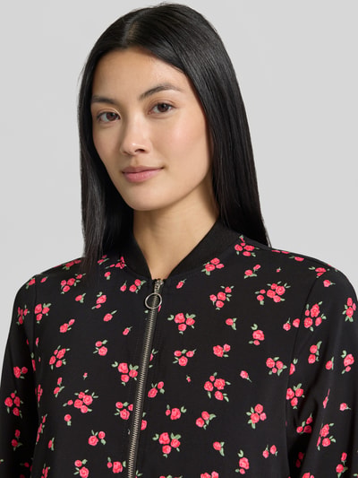 Frauenmodel trägt Regular Fit Blouson mit Allover-Muster Modell 'COCO' von VERO MODA mit rosa Blumen auf schwarzem Stoff, Nahaufnahme Oberkörper. Damen Bomberjacke / Blouson.