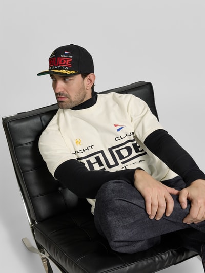 Männermodel trägt Relaxed Fit T-Shirt mit Logo-Print von RHUDE aus reiner Baumwolle im Kurzarm-Design, Ganzkörperansicht von vorne.