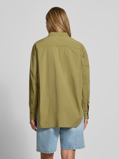 Frauenmodel trägt Relaxed Fit Hemdbluse aus reiner Baumwolle Modell 'JAMIE' von JJXX in Oliv mit feinen Streifen, Rückenansicht, Ganzkörperansicht Rückansicht. Hemdblusenkragen, langärmliges Design, aufgesetzte Brusttasche, durchgehende Knopfleiste, überschnittene Schultern, 77 cm Rückenlänge bei Größe S, 56 cm Ärmellänge bei Größe S.