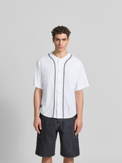 Männermodel trägt Freizeithemd in kurzärmeligem Design von Kenzo in Weiß mit schwarzer Zierlinie, Reine Baumwolle, Relaxed-Fit, Knopfleiste, Rundhalsausschnitt, Ganzkörperansicht von vorne.