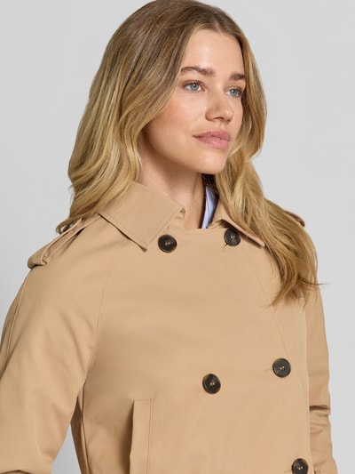 Frauenmodel trägt Trench Jacke mit Eingrifftaschen und Kentkragen von monari in Beige mit 2-reihige-Knopfleiste, Nahaufnahme Oberkörper. Gerader-Schnitt, Schulterriegel, Riegel an Ärmel und Seite, Rückenlänge 52 cm, Schulterbreite 47 cm, Brustweite 47 cm, Ärmellänge 57 cm bei Größe 36.