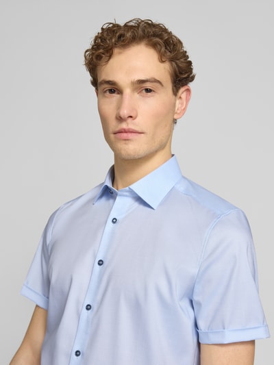 Männermodel trägt Slim Fit Business-Hemd mit Kentkragen von OLYMP Level Five in Hellblau, glatte Textur, Nahaufnahme Oberkörper. Baumwoll-Elasthan-Mix, kurze Ärmel, Knopfleiste, Business-Stil.