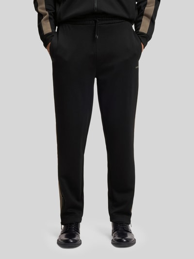 Männermodel trägt Relaxed Fit Jogginghose mit Galonstreifen Modell 'DOLOS' von HUGO, unifarben, Sweatmaterial, seitliche Eingrifftaschen, Nahaufnahme Vorderansicht.