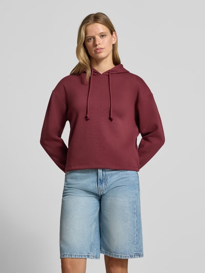 Frauenmodel trägt Regular Fit Hoodie aus Baumwoll-Mix Modell 'CHILLI' von PIECES in Dunkelrot, kombiniert mit hellblauen Shorts, Nahaufnahme Oberkörper. Damen Hoodie von PIECES.