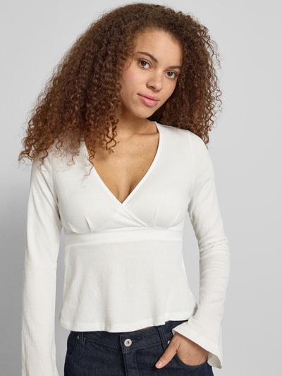 Frauenmodel trägt Regular Fit Langarmshirt in Wickel-Optik Modell 'PELLY' von Only mit Struktur-Muster, V-Ausschnitt, Trompetenärmel, Nahaufnahme Oberkörper.