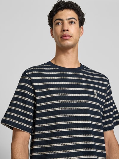 Männermodel trägt Strukturiertes T-Shirt mit Logostickerei auf der Brust von REVIEW in Dunkelblau mit Strukturmuster, Reine Baumwolle, Gerader-Schnitt, Rundhalsausschnitt, Label-Stitching, Lochstickerei auf der Brust, Rückenlänge 70 cm in Größe M, Nahaufnahme Oberkörper.
