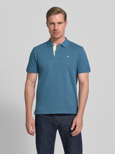 Męski model nosi Regular Fit Poloshirt aus reiner Baumwolle von Tom Tailor, efekt: jednolity kolor, wyhaftowane logo, kołnierzyk polo, zapięcie na 2 guziki, krótki rękaw, wykończenie: z rozcięciami po bokach, wykończenie materiału: pika, materiał: bawełna, Ganzkörperansicht von vorne.