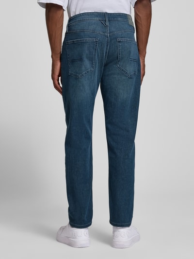 Männermodel trägt Tapered Fit Jeans aus Baumwoll-Mix von s.Oliver RED LABEL in Blau, sichtbare Nahtdetails, Ganzkörperansicht Rückansicht.