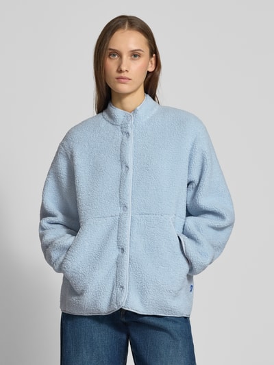 Frauenmodel trägt hellblaue Relaxed Fit Fleecejacke mit Stehkragen Modell 'VERA' von JJXX aus Teddyfell, Knopfleiste, Eingrifftaschen, Rückenlänge 57 cm, Schulterbreite 41 cm, Brustweite 53 cm, Ärmellänge 54 cm, Ganzkörperansicht von vorne.