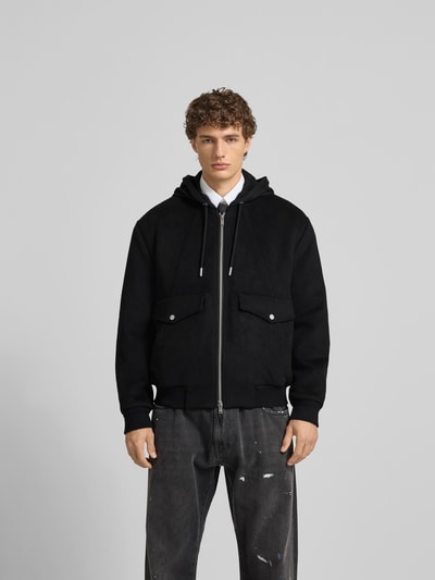 Männermodel trägt Jacke mit Kapuze von Moose Knuckles aus schwarzem Woll-Mix mit Pattentaschen und Reißverschluss, Ganzkörperansicht von vorne
