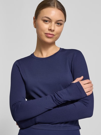 Frauenmodel trägt Cropped Longsleeve mit Rundhalsausschnitt Modell 'Feather' von Fabletics in Dunkelblau, elastischer Stoff, Nahaufnahme Oberkörper.