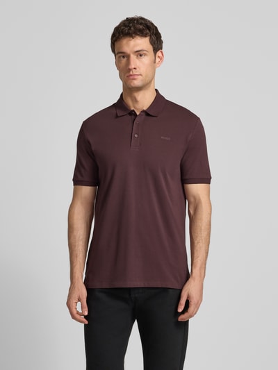 Männermodel trägt Regular Fit Poloshirt aus reiner Baumwolle Modell 'DONOS222' von HUGO, unifarben, Label-Print, Ganzkörperansicht von vorne.