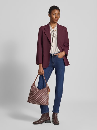 Frauenmodel trägt Shoulder Bag mit Reißverschluss Modell 'PORTA' von MANGO, Allover-Logo-Print, Braun, Ganzkörperansicht von vorne.