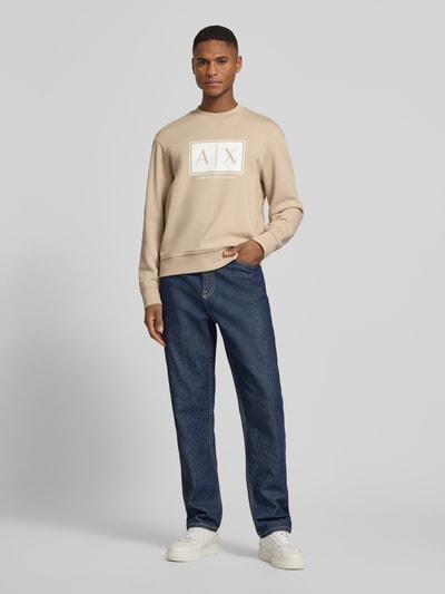 Männermodel trägt Sweatshirt mit Logo-Print und Rundhalsausschnitt von ARMANI EXCHANGE in Beige, Loose Fit, Baumwolle, Jeans, Ganzkörperansicht von vorne.