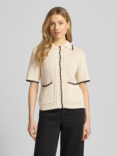 Frauenmodel trägt Regular Fit Cardigan mit Lochmuster Modell 'Muno' von B.Young aus reiner Baumwolle, kurzärmelig, Strick-Optik, Umlegekragen, aufgesetzte Taschen, durchgehende Knopfleiste, hellbeige mit dunklen Kanten, Strukturmuster. Nahaufnahme Oberkörper.