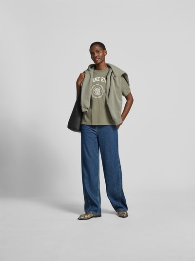 Frauenmodel trägt Oversized Sweatshirt mit Logo-Detail von Anine Bing aus reiner Baumwolle im Oversized-Fit mit Rundhalsausschnitt, elastische Abschlüsse, Rückenlänge bei Größe S 62 cm, in khaki mit weißem Logo-Print, kombiniert mit blauer Jeans, Ganzkörperansicht von vorne.